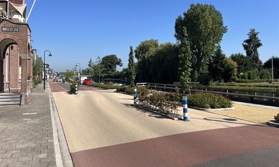 Een weg met veel ruimte voor de fiets, aangezien het onderdeel is van een regionale doorfietsroute. Met blauwe lucht en groene bomen op de achtergrond. 